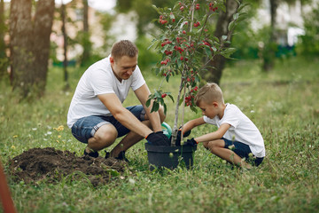 Naklejka na ściany i meble Family on a yard. Father with son planting a tree. Boy with a green funnel