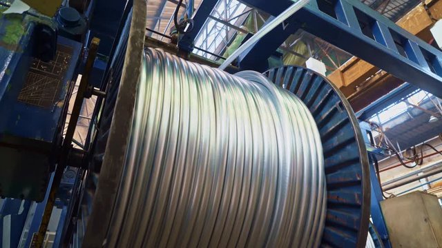 A huge bobbin unwinds a wire in a cable factory. Products are used in energy, transport, construction, engineering, nuclear, defense, oil and gas industries.