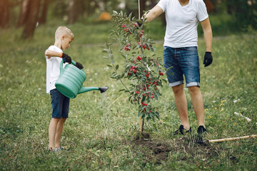 Family on a yard. Father with son planting a tree. Boy with a green funnel