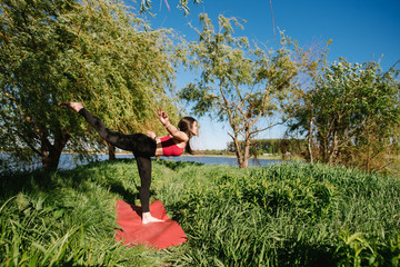 young sport woman practicing yoga outdoors at the lakeshore
