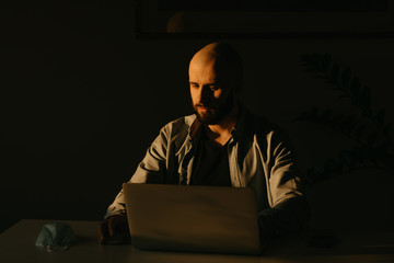 A caucasian man with a beard working remotely on his laptop during the quarantine to avoid the...