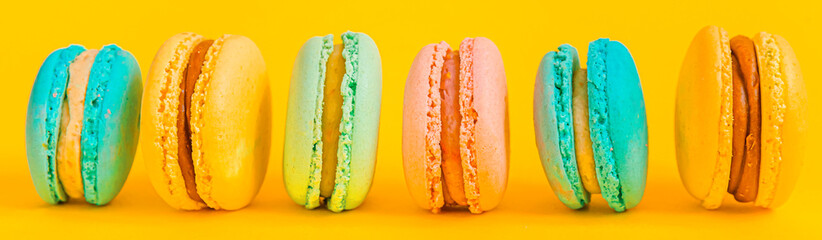 Sweet almond colorful unicorn pink blue yellow green macaron or macaroon dessert cake isolated on trendy yellow modern fashion background. French sweet cookie. Minimal food bakery concept Banner
