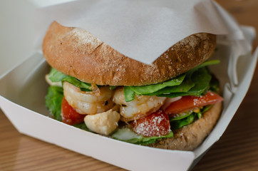 hamburger with dark flour with vegetables and shrimp on a wooden background