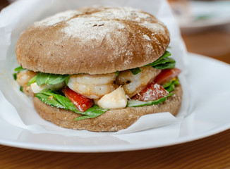 hamburger with dark flour with vegetables and shrimp on a wooden background