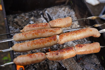 Close up of toasted sausages on skewers. Succulent kupaty roasting on chargrill. Concept of picnic outdoor.
