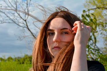 Girl is standing with blowing hair in  nature, hand on head