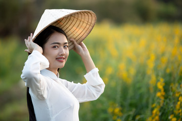 Vietnamese girl wearing a hat and riding a bicycle in a yellow flower bed