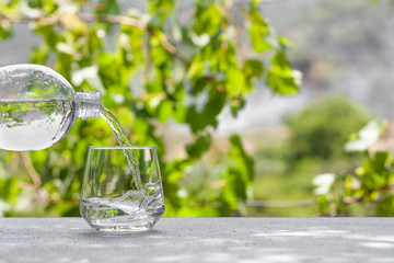 Fersh, clean, drink water pouring in to glass from a plastic bottle. Select focus blurred nature background. Healthy lifestyle, water balance control, skin care concept