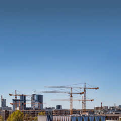 Fototapeta na wymiar A modern real estate development metropol cityscape with skyscrapers being built by several cranes in the bottm and a lot of copy space on a clear gradient blue sky in the upper part