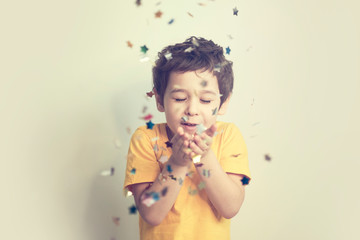 Obraz na płótnie Canvas happy birthday child. Photo of charming cute fascinating nice little boy blowing confetti at you to show her festive mood with emotional face expression.