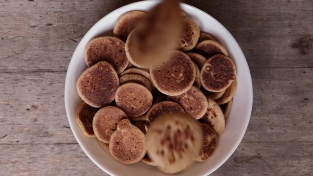 Mini pancakes falling in bowl in slow motion, top view. Tiny pancake cereal - trendy quarantine food. Homemade breackfast.