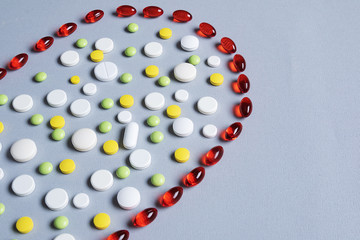 red vitamin capsules with pills of different shapes and colors on a gray background. Pharmaceutical concept.