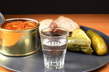 A glass of vodka and an appetizer for alcoholic drinks (canned sprats, pickled cucumbers and bread).