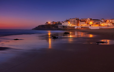 Amazing landscape of the Atlantic ocean coast at dusk. Night view on the village in lights, reflecting on a sandy beach. Long exposure image. Beach of Praia das Macas. Sintra. Portugal.