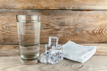Glass with foda, next to ice cubes and a towel layer on a wooden background.
