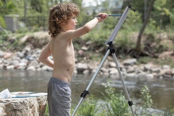 A boy is painting outside in the woods, the kid is shirtless in the summer. He is creative, having...
