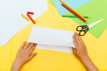 young child boy hands does white paper fly plane on yellow table step to step