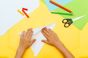 young child boy hands does white paper fly plane on yellow table step to step