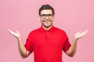 Portrait of a joyful young man pointing fingers away at copy space on his palm isolated over pink background.