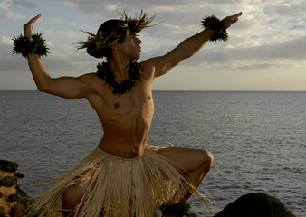 Male Hula Dancer poses on the beach and is almost silhouetted as the sun begins to set. 
