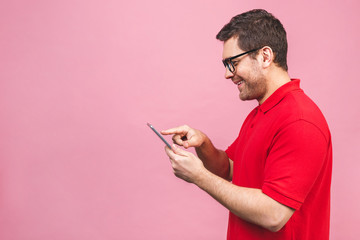 Image of happy young bearded man standing over pink background isolated. Using tablet computer.