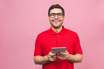 Image of happy young bearded man standing over pink background isolated. Looking camera using tablet computer.