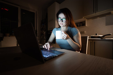 Caucasian woman in glasses sits at a wireless computer in the kitchen. A student prepares for the...