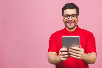 Image of happy young bearded man standing over pink background isolated. Using tablet computer.