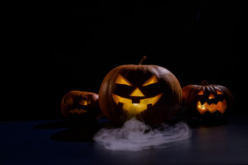 Halloween card. jack o lantern with candles glow on a black background. A row of creepy pumpkins with carved grimaces smokes in the dark.
