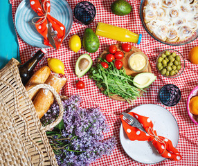 Homemade picnic with fresh fruits, vegetables, salad, orange juice, flowers and baguette on a red plaid. Beautiful still life.