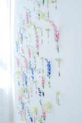 Flower multicolored installation. A lot of flowers of different colors fixed on a wall of white, blue, pink, yellow colors. Decoration of the walls. Vintage home decor background.