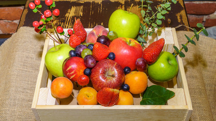 Set of berries and fruits in wooden box. Apple, strawberry, grape, berry and peach on a red brick...