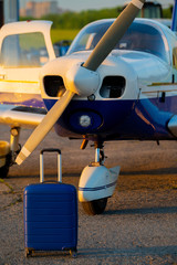 A blue suitcase and a landed small private jet. Four-seater plane with a propeller for the air taxi. Self travel concept. Airplane for VIP persons.