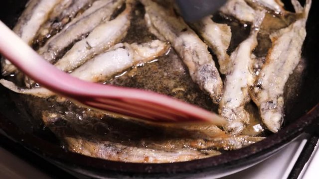 The process of preparing fried capelin fish in vegetable oil. Turning fried fish with shoulder blades. Cooking