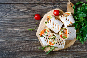 Fresh tortilla wraps with chicken, mushrooms and fresh vegetables on wooden board. Chicken Mexican burrito. Tasty appetizer. Dishes from pita bread. Healthy food concept.