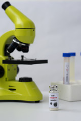 Anti-COVID-19 vaccine, microscope and tubes with blood positive to coronavirus.  Portrait orientation. White background.