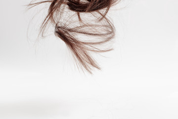 hair falls from top to bottom on a light gray background. Curls of brown hair in parts descend from above on a white background