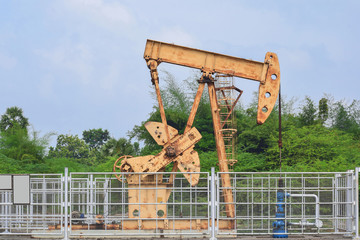 Old rusty oil pump jack extracting crude oil and natural gas from well in green background