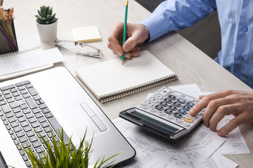 Man hand using calculator and writing make note with calculate about cost and taxes at home office....
