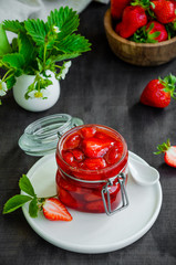 Homemade strawberry jam in a glass jar with fresh strawberries on a dark wooden background. Rustic style. Vertical orientation.