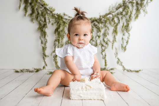 Baby girl first birthday cake smash on a white wood set in a white background and white cake