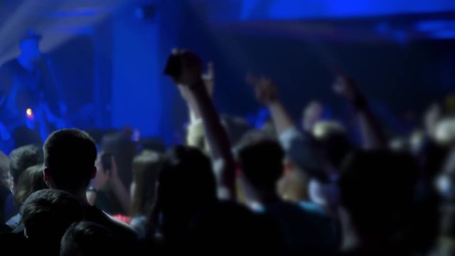 Slow motion: people crowd silhouette partying, cheering and jumping at rock concert in front of stage of nightclub. Bright colorful stage lighting. Nightlife and entertainment concept