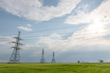 High-voltage power lines passing through a green field of wheat, on the background of a cloudy sky