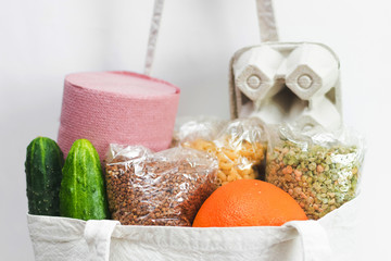 Close up cloth bag with eggs in box, buckwheat, oatmeal, pea, cucumbers, orange, pasta and toilet paper. Home food delivery ordered online on white background. Donation for coronavirus quarantine.