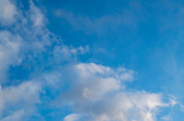 Clouds in a blue sky with a Crescent moon in the distance.