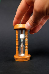 A male hand holds a wooden hourglass on a black background.