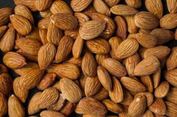 Almond close-up on a black background. Different angles of popular tree nuts, healthy and nutritious ingredient. Almond in a black pan high angle view on a white wooden background