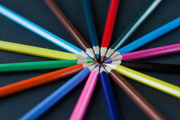 Circle of colour pencils on black background.Close up. Many different colored pencils on dark purple background.Colorful pencil.