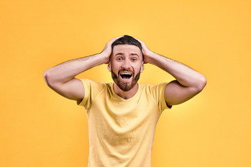 Crazy emotions of wonder! Portrait of a handsome man in a yellow T-shirt holding his head in joy, wonder and laughter.