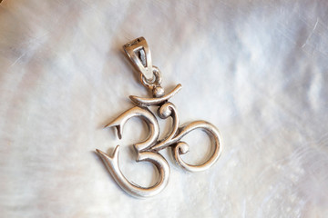 Sterling siver pendant in the shape of om on white shell background